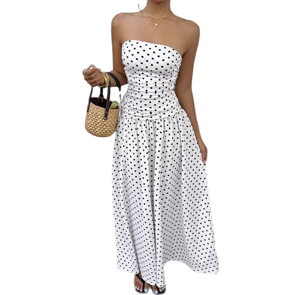 Polka-dot strapless maxi dress with ruched waist in white and black; paired with straw handbag.