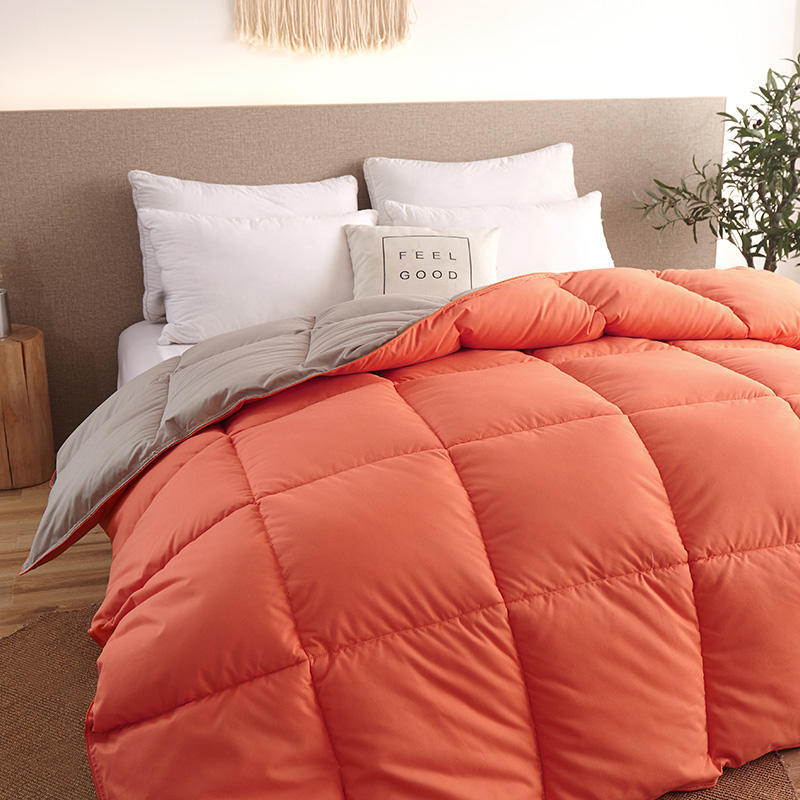 Goose down duvet on bed; warm orange quilt with gray reverse and white pillows in a cozy bedroom.