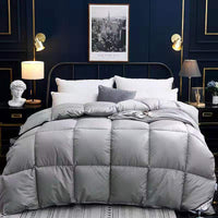Down duvet on bed in light gray with quilted square stitching, winter comforter