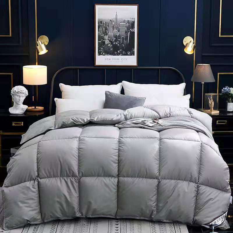 Down duvet on bed in light gray with quilted square stitching, winter comforter