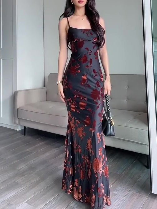 Flocked strappy maxi dress in black with red floral flocking, floor-length, worn by a model with a black handbag.