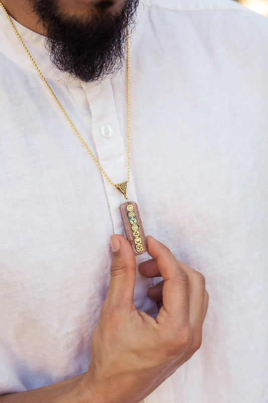 Seven chakra orgone copper pendant with chain, featuring colorful chakra stones and intricate design, on a black background.