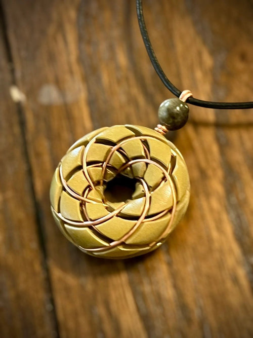 Brass Torus Vortex pendant with Libyan Desert Glass Orgonite necklace and Rodin Coil by Ancient Energy, close-up view of the jewelry piece.