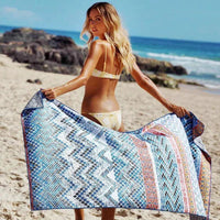 Mandotos SwiftDry patterned beach towel with colorful geometric design spread on sandy beach.